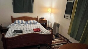 Quarto com cama de madeira, mesa de cabeceira, luminária, espelho e janela com cortinas.