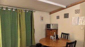 Uma área de refeições com uma mesa e cadeiras de madeira, um micro-ondas sobre um armário de madeira, e uma cortina verde com listras amarelas.