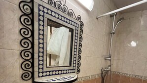Uma casa de banho com uma pia branca, um espelho com moldura decorativa e um chuveiro.