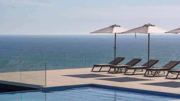 A poolside area with lounge chairs and umbrellas, overlooking a body of water. - HOTEL BOUTIQUE FARO SILLEIRO (Baiona)