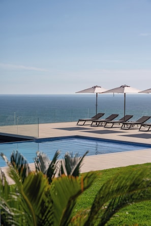 A poolside area with lounge chairs and umbrellas, overlooking a body of water. - HOTEL BOUTIQUE FARO SILLEIRO (Baiona)