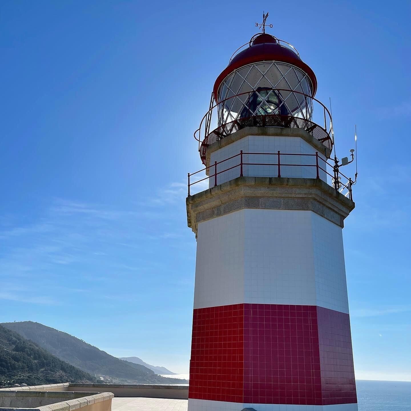 A lighthouse with a red and white color scheme, a metal railing, and a clear view of the surrounding landscape.
