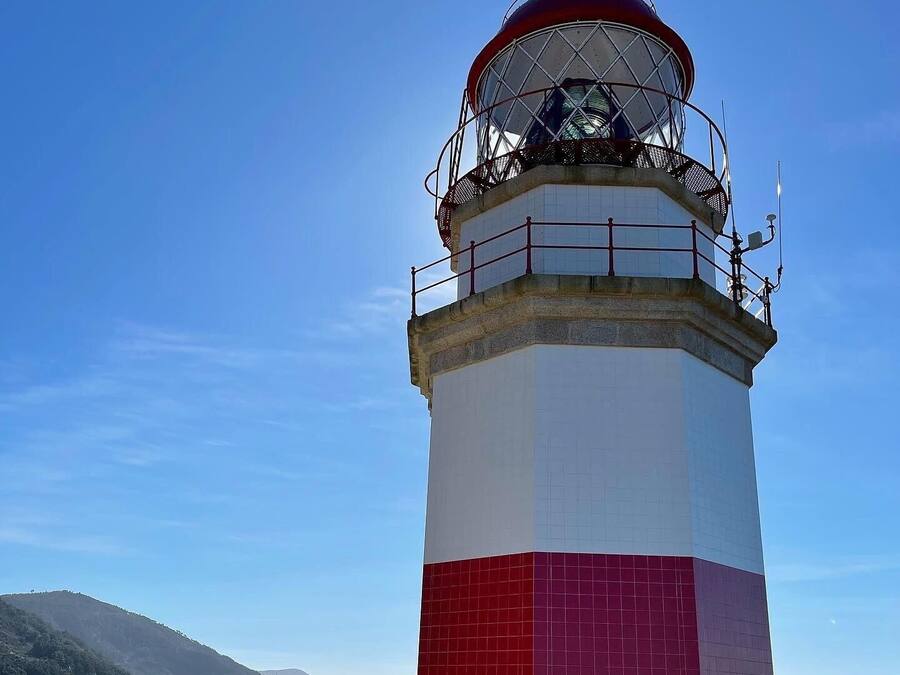 A lighthouse with a red and white color scheme, a metal railing, and a clear view of the surrounding landscape.