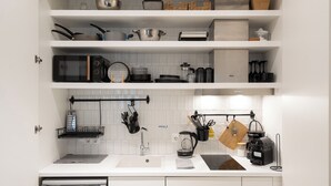 A modern kitchen with white cabinetry, a built-in oven, a coffee machine, and various kitchen utensils. - Modern Studio, Walking distance to Kolonaki & The Ilisian (Athens)