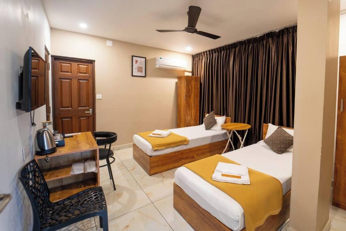 A hotel room with two beds, a desk, a chair, a ceiling fan, and a television.