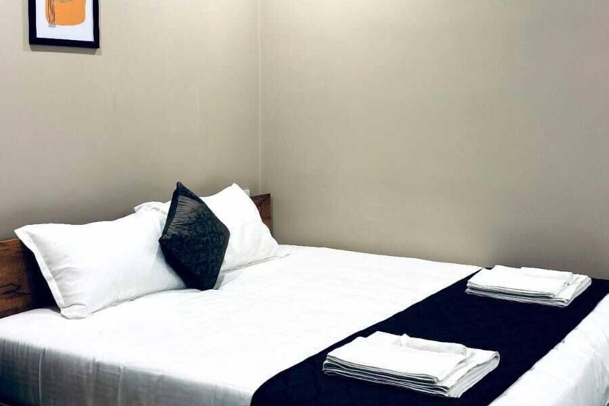 A neatly made bed with white linens and a dark headboard, a ceiling fan, and a framed abstract artwork on the wall.