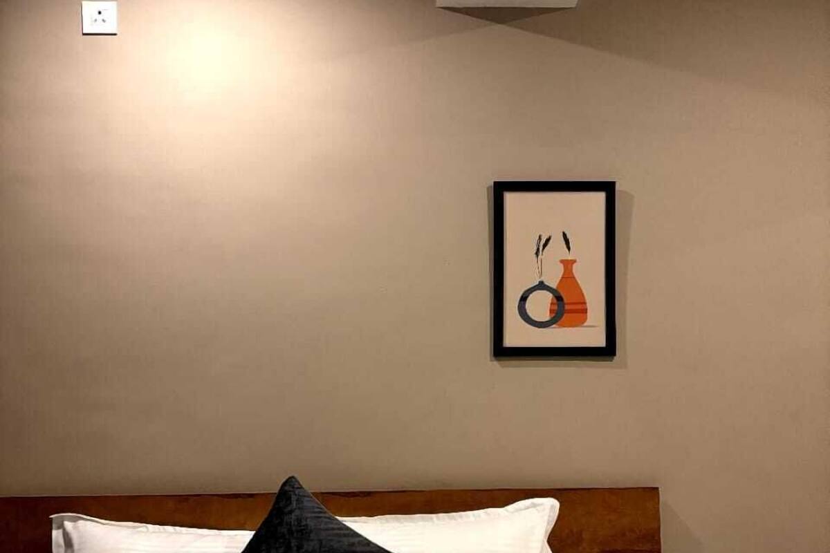 A hotel room with a bed, white bedding, a dark pillow, and a framed picture on the wall.