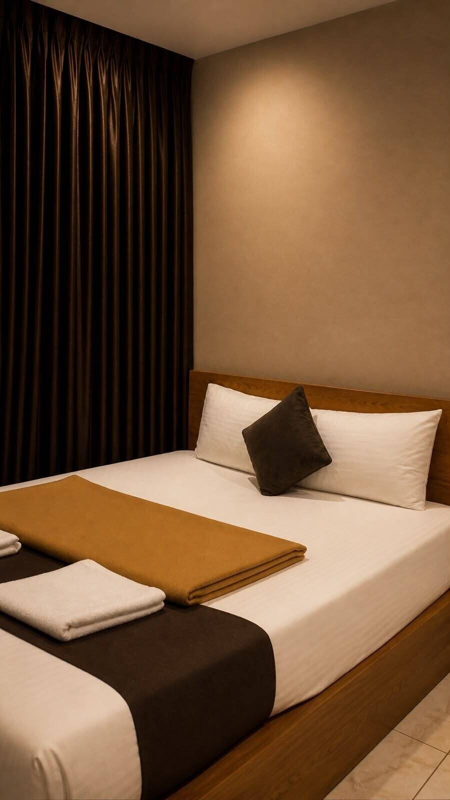 A hotel room with a bed, a brown throw blanket, and a white pillow.
