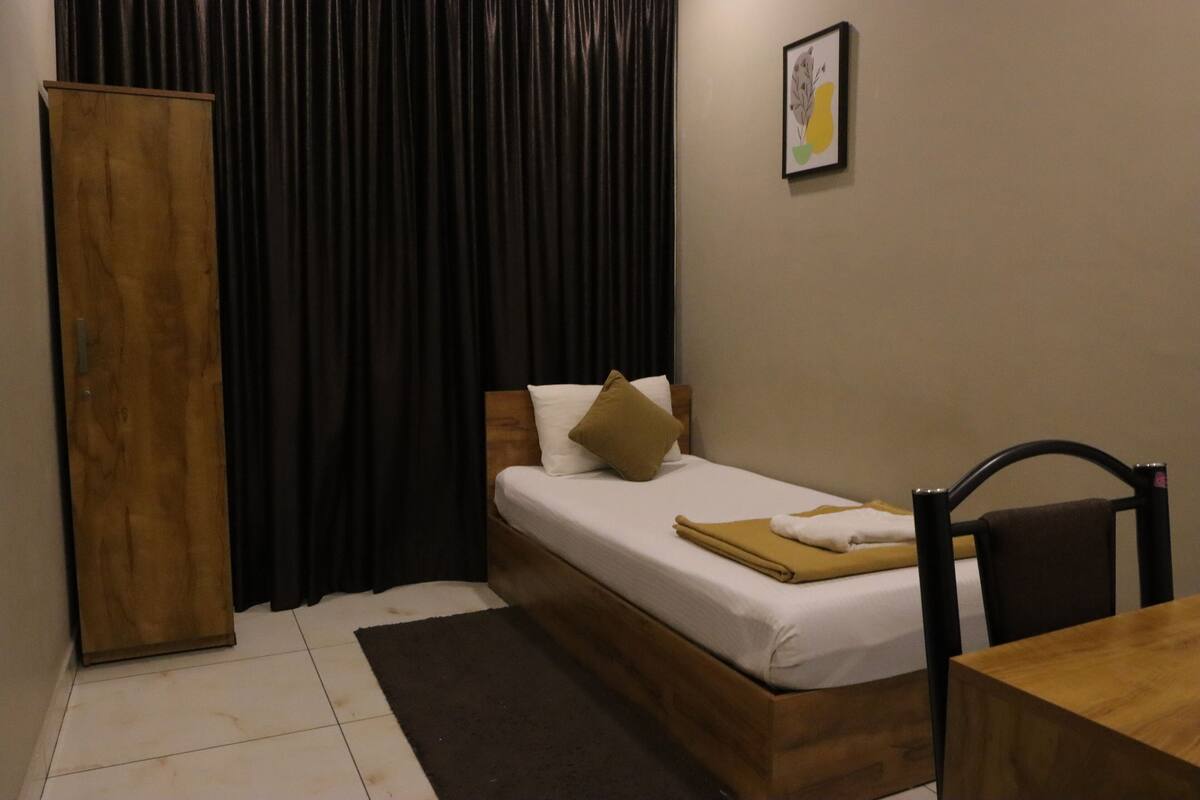 A bedroom with a bed, a wooden wardrobe, a table, and a chair.