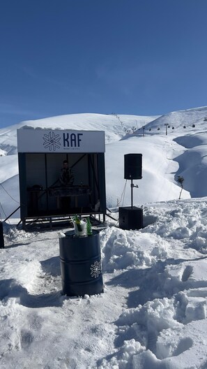 A snow-covered outdoor area with a KAF sign, a speaker, and a barrel with bottles. - KAF MOUNT ERCİYES (Hacilar)