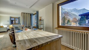 Ein stilvoller Essbereich mit Holztisch, gedeckt für vier Personen, einer Couch und Blick auf schneebedeckte Berge durch ein großes Fenster.