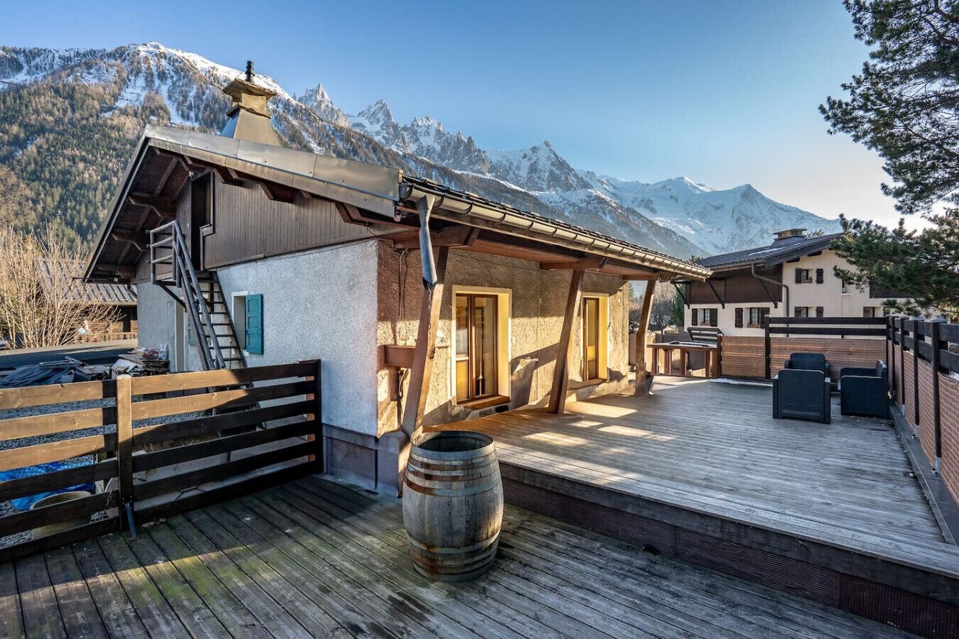 Un chalet rustique doté d’une terrasse en bois, d’une barrique et surplombant un paysage montagneux.