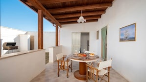 Un espace extérieur abrité, aménagé pour les repas, avec une table ronde, des chaises et un barbecue.