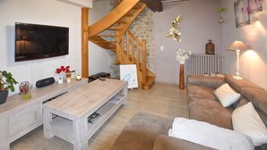 A living room with a wooden coffee table, a brown sofa, a TV mounted on the wall, a wooden staircase, and a radiator. - Luxurious home in Vedène with WiFi (Vedène)