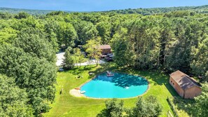 A large, circular swimming pool surrounded by a well-maintained lawn and dense forest.