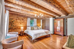 A log cabin bedroom with a wooden bed, a nightstand, a chair, and a wardrobe.