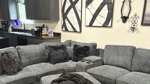 A sectional sofa with a dark throw blanket, a black and white abstract painting, and a decorative wall piece in a living room. - Charming 3-bedroom house with WiFi and AC in West Monroe (West Monroe)