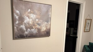 A room with a large abstract painting on the wall, a green chair, and a doorway leading to another room. - Charming 3-bedroom house with WiFi and AC in West Monroe (West Monroe)