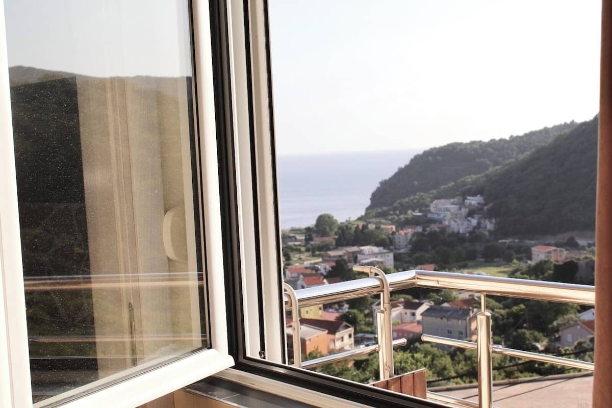 A window with a view of a coastal town and hills.
