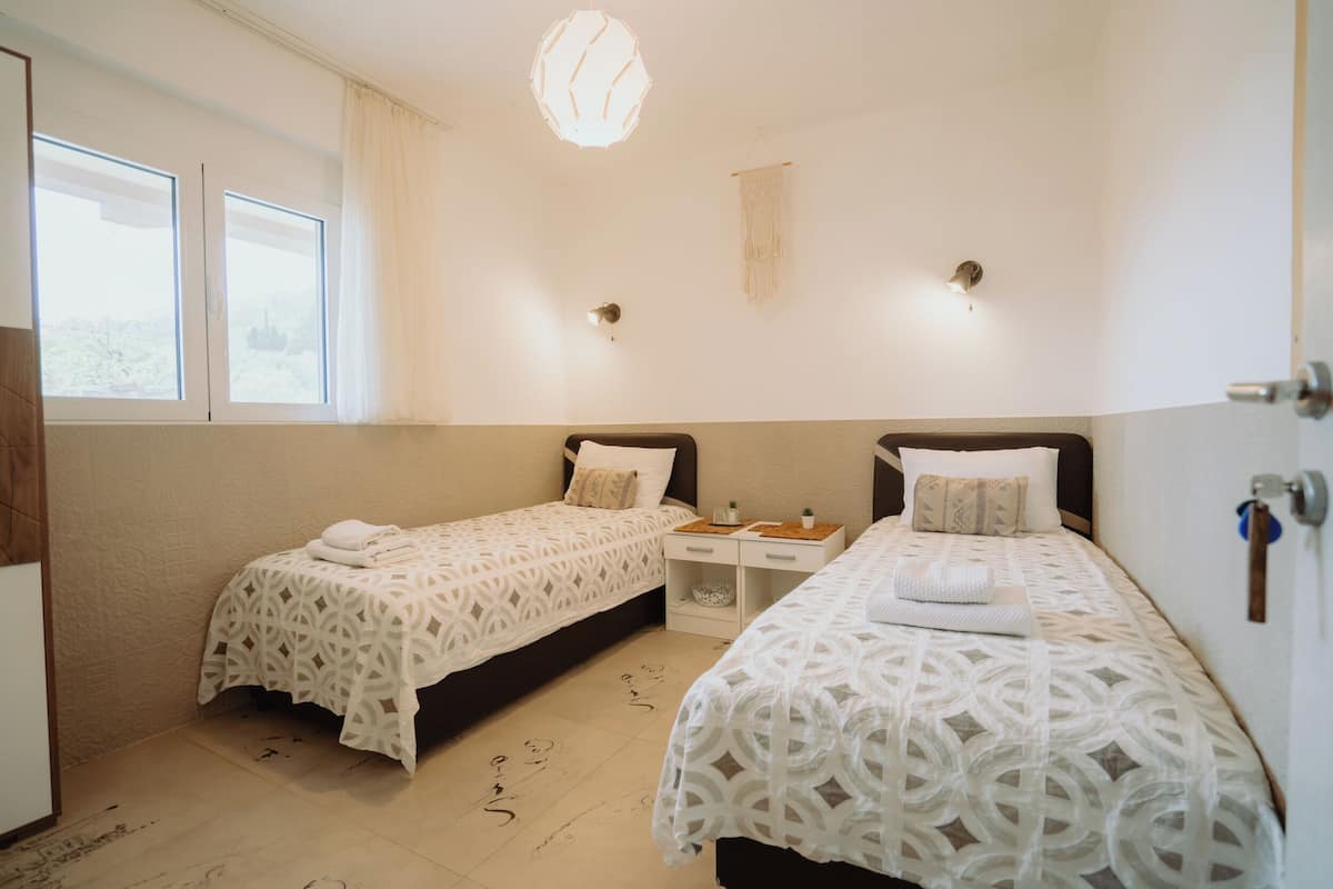 A room with two beds, a small table, and a hanging light fixture.