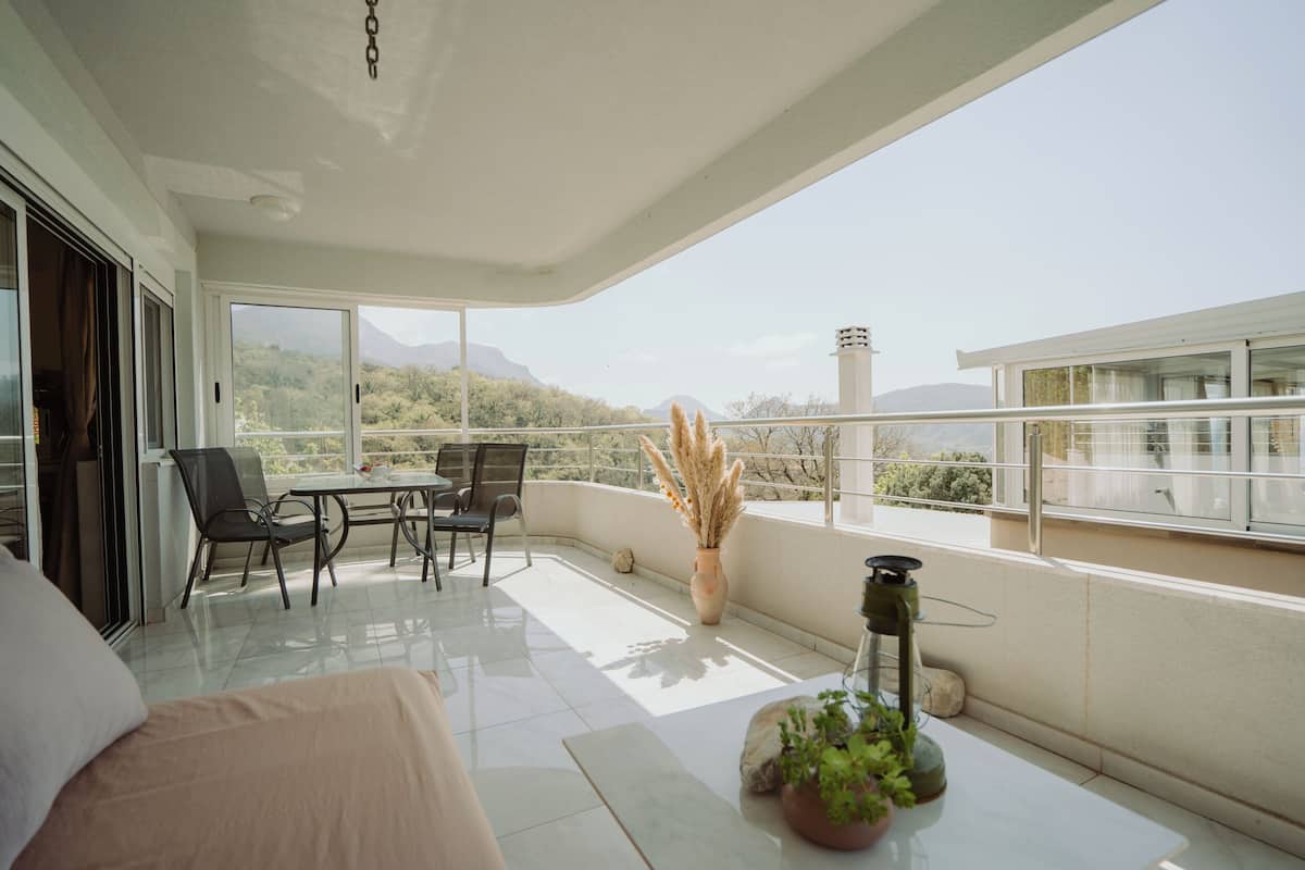 A balcony with a table and chairs, a potted plant, and a view of mountains.