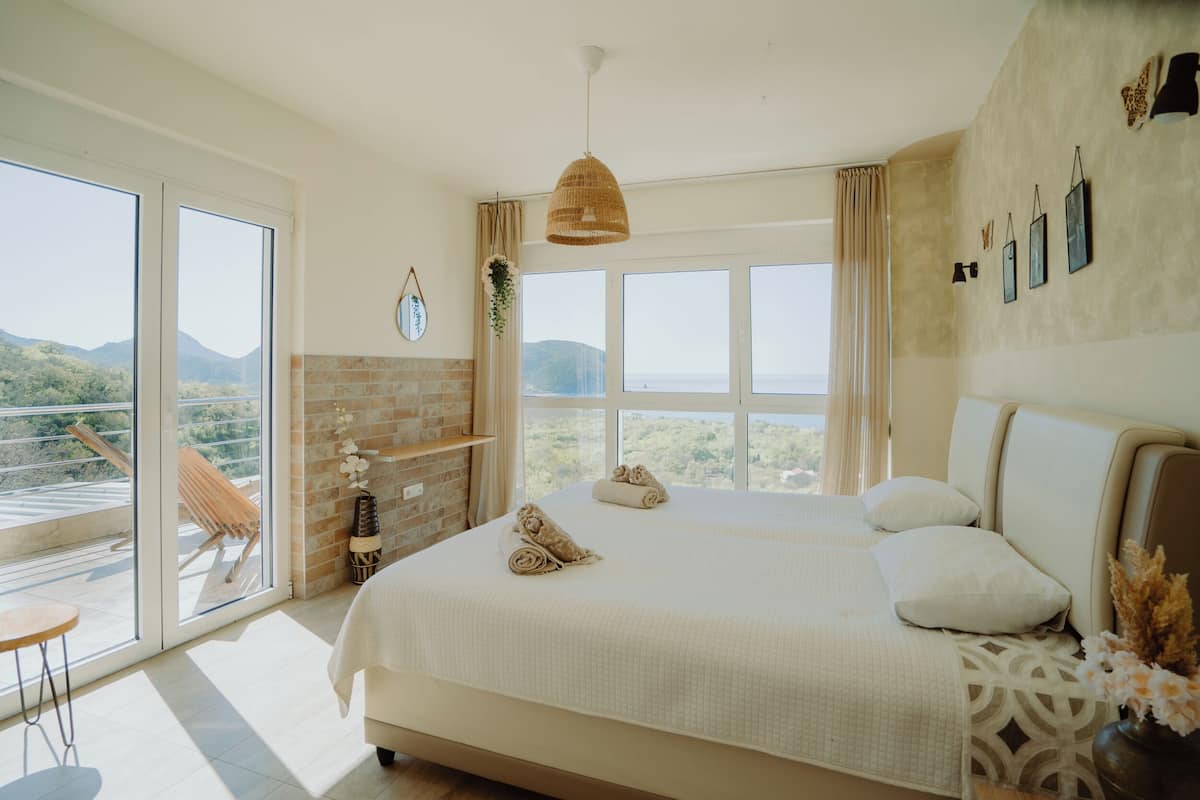 A spacious bedroom with a large bed, a balcony with a view, and a brick wall.