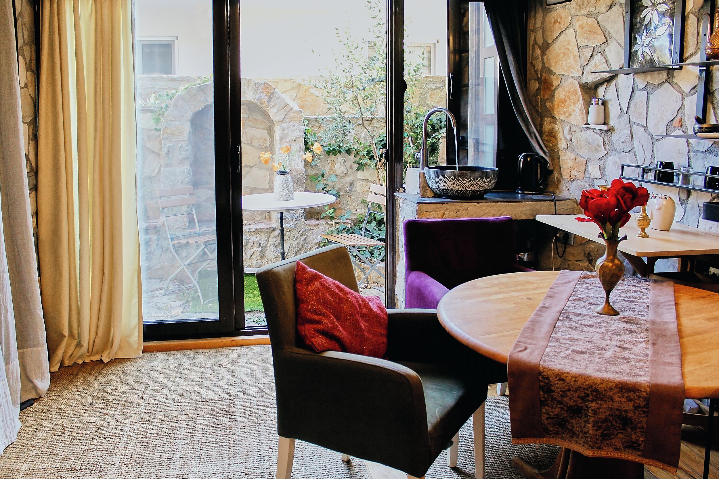 A cozy room with a stone wall, a dining table with a vase of flowers, and a chair with a red pillow.