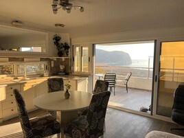 Cocina moderna con comedor, puertas de vidrio correderas que dan a un balcón con vistas al mar.