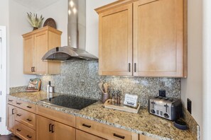 A kitchen with granite countertops, wooden cabinets, a stainless steel range hood, a toaster, and a coffee maker.