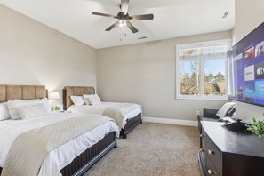 A bedroom with two beds, a ceiling fan, a large window, and a TV on a dresser.