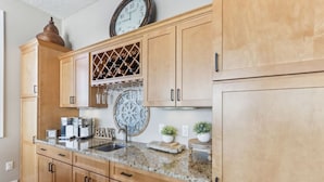 A kitchen with wooden cabinets, a granite countertop, a wine rack, a clock, and a coffee maker. - Penthouse Paradise at Delton Grand (Wisconsin Dells)