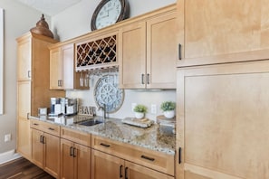 A kitchen with wooden cabinets, a granite countertop, a wine rack, a clock, and a coffee maker.