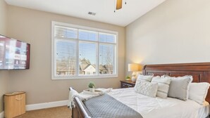 A bedroom with a large bed, a bedside table with a lamp, a TV mounted on the wall, and a window with blinds. - Penthouse Paradise at Delton Grand (Wisconsin Dells)