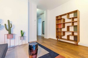 Ein modernes Wohnzimmer mit Holzboden, einer großen Bücherwand und zwei Kübelpflanzen.