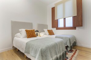 A bedroom with two beds, a window with wooden shutters, and a patterned rug on the floor. - Elegant 4-Bedroom Apartment in the Heart of Madrid (Madrid)