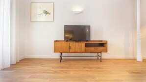 Una habitación con piso de madera, un televisor sobre un mueble de madera y un cuadro en la pared.