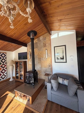 A cozy living room with a stone wall, a fireplace, a sofa, and a television. - Welcome to Heron's Hearth (Cape Meares)
