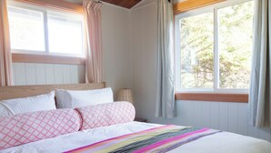 A bedroom with a bed, a window with curtains, and a view of trees outside.