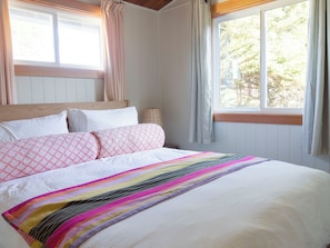 A bedroom with a bed, a window with curtains, and a view of trees outside.