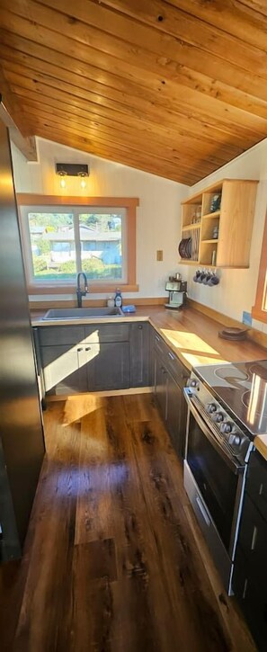 A kitchen with wooden flooring, a stainless steel stove, and a built-in oven. - Welcome to Heron's Hearth (Cape Meares)