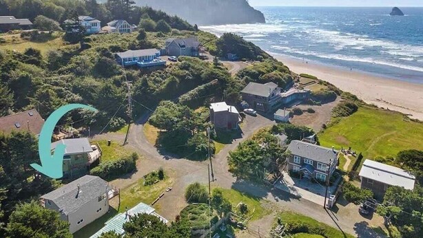 Vista aérea de una zona residencial costera con casas, una playa y un acantilado cubierto de bosque.