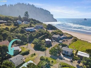 An aerial view of a coastal residential area with houses, a beach, and a forested cliff.