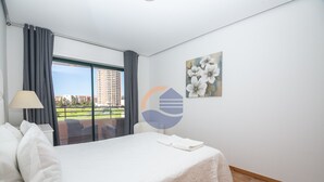 Ein Hotelzimmer mit Bett, Fenster mit Vorhängen, einem Gemälde und Blick auf Gebäude.