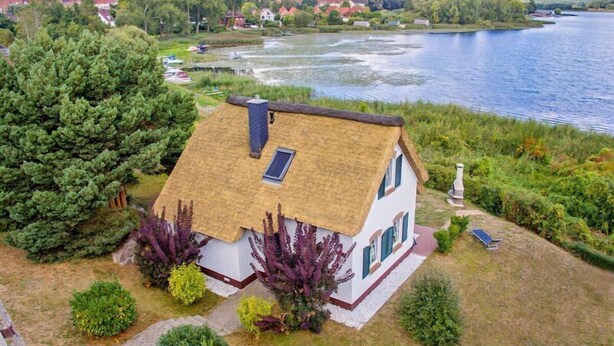 Een huis met rieten dak, omgeven door weelderige begroeiing en een meer.
