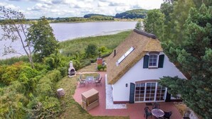 Een rieten huis met een terras, een barbecue en uitzicht op een meer.