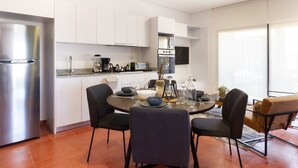 Eine moderne Küche mit weißen Schränken, einem Edelstahlkühlschrank und einem Essbereich mit rundem Tisch und vier Stühlen.
