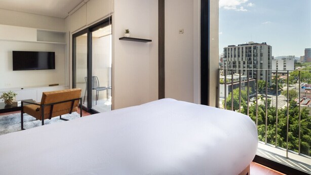 Ein modernes Hotelzimmer mit einem großen Bett, einem Schreibtisch und einem an der Wand befestigten Fernseher.