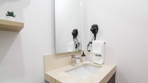 Ein Badezimmer mit einer beige farbenen Waschtischplatte, einem Waschbecken, einem Spiegel, einem Haartrockner und einem Handtuchhalter.