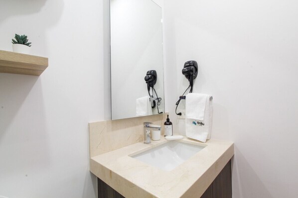 A bathroom with a beige countertop, a sink, a mirror, a hairdryer, and a towel rack.
