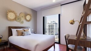 Ein Schlafzimmer mit einem großen Bett, einem Schreibtisch mit Stuhl und Blick auf Gebäude durch das Fenster.